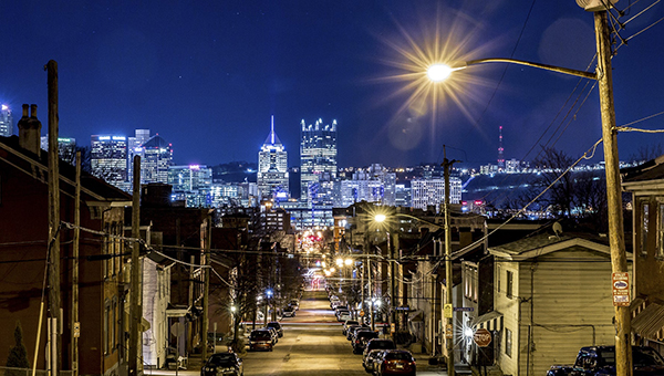 Image of a Pittsburgh street at night with the Pittsburgh skyline in the distance
